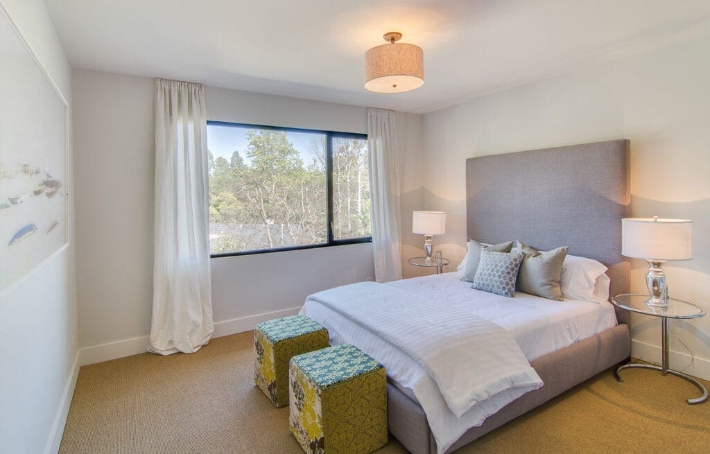 A bedroom with a bed, two stools and a window.