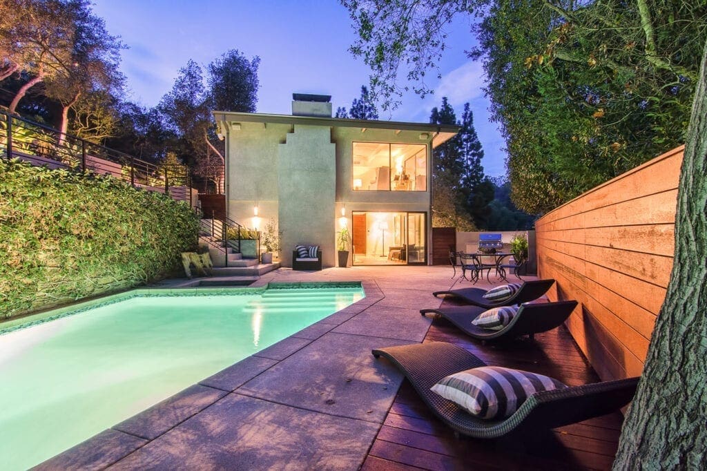 A pool and some chairs in front of a house.