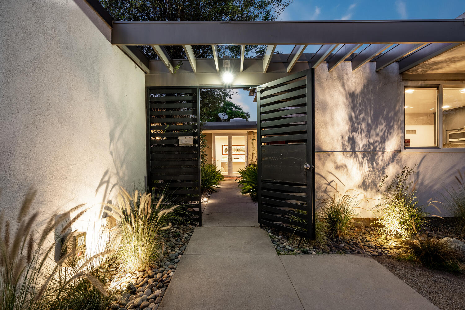 A walkway with two black gates leading to the side of a house.