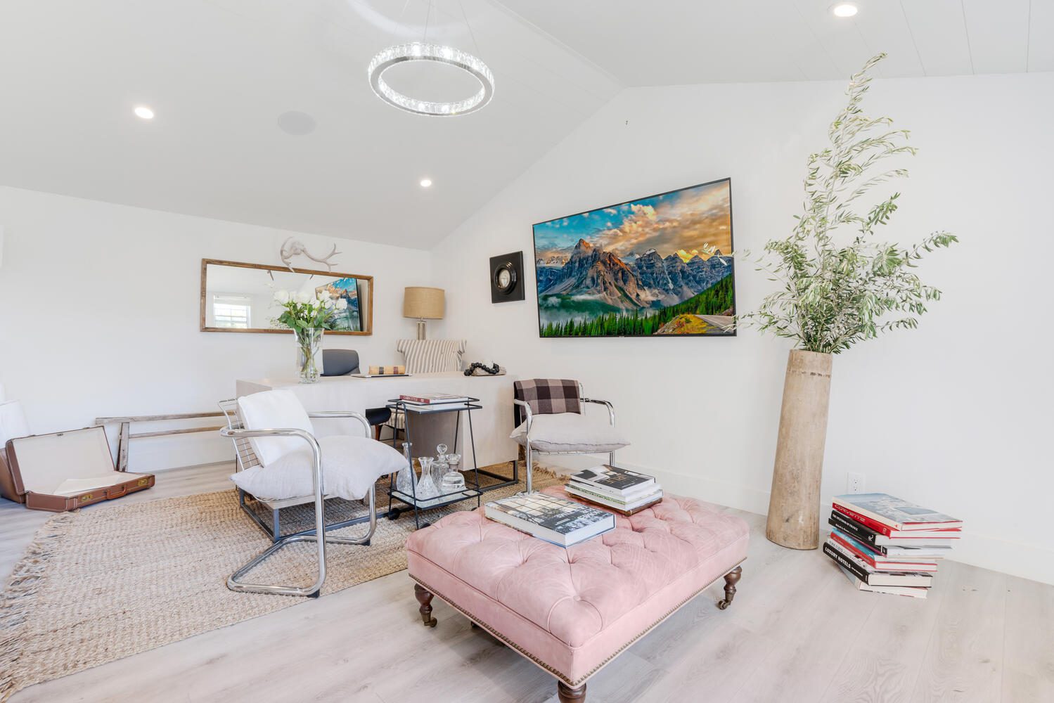 A living room with a pink ottoman and white walls.