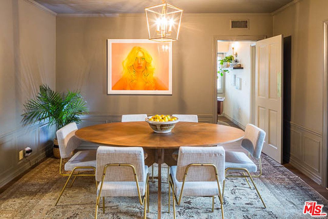 A dining room table with white chairs and a painting on the wall.