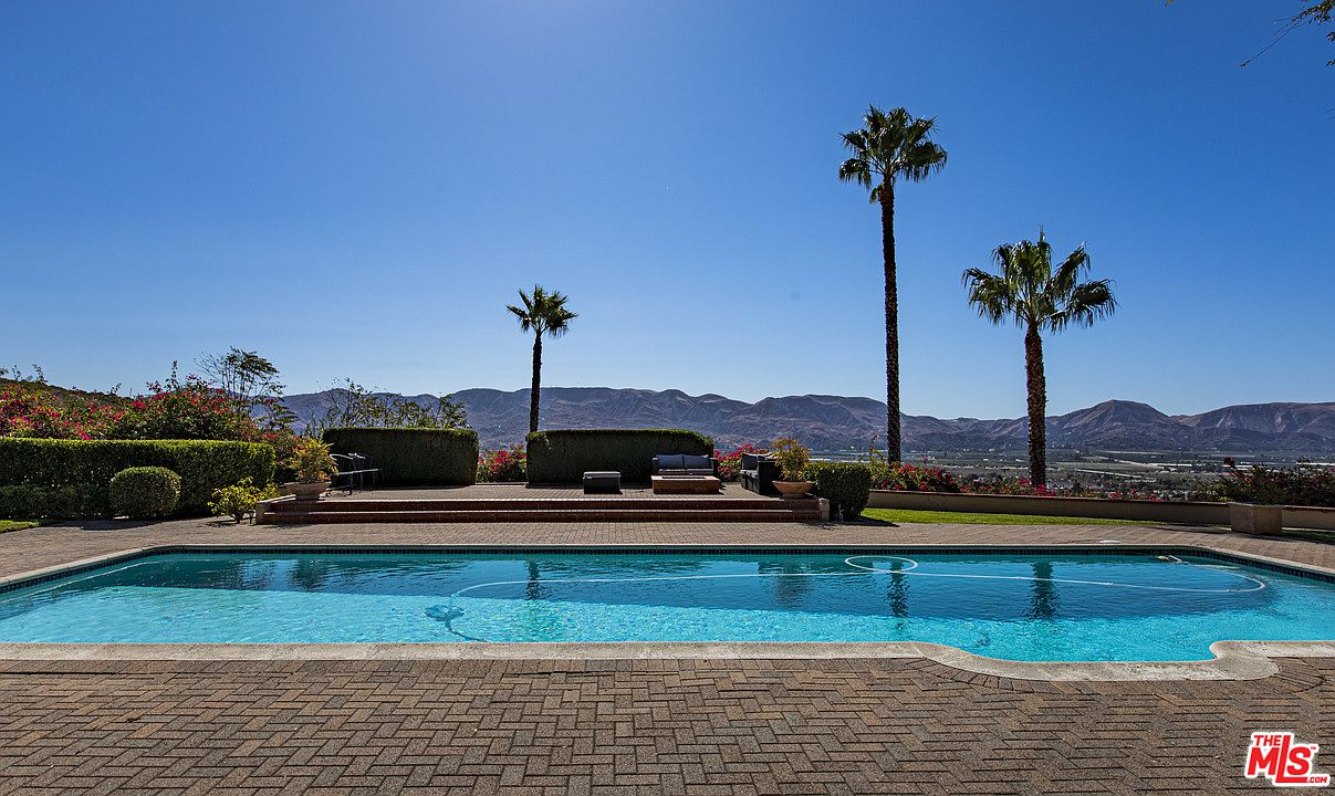 A pool with palm trees and mountains in the background.