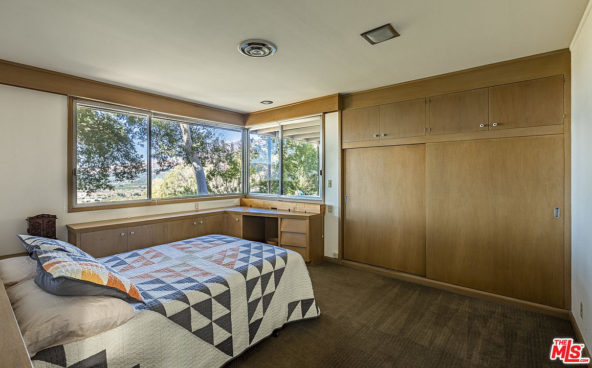 A bedroom with a bed, desk and large window.