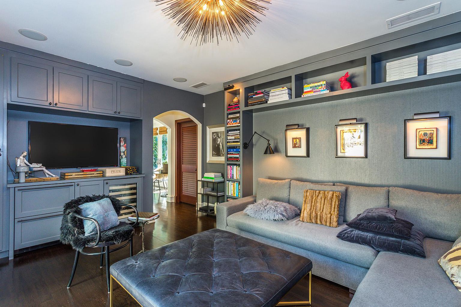 A living room with a couch, ottoman and television.