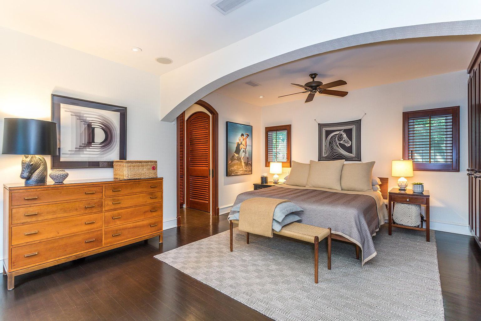 A bedroom with a bed, dresser and arched doorway.