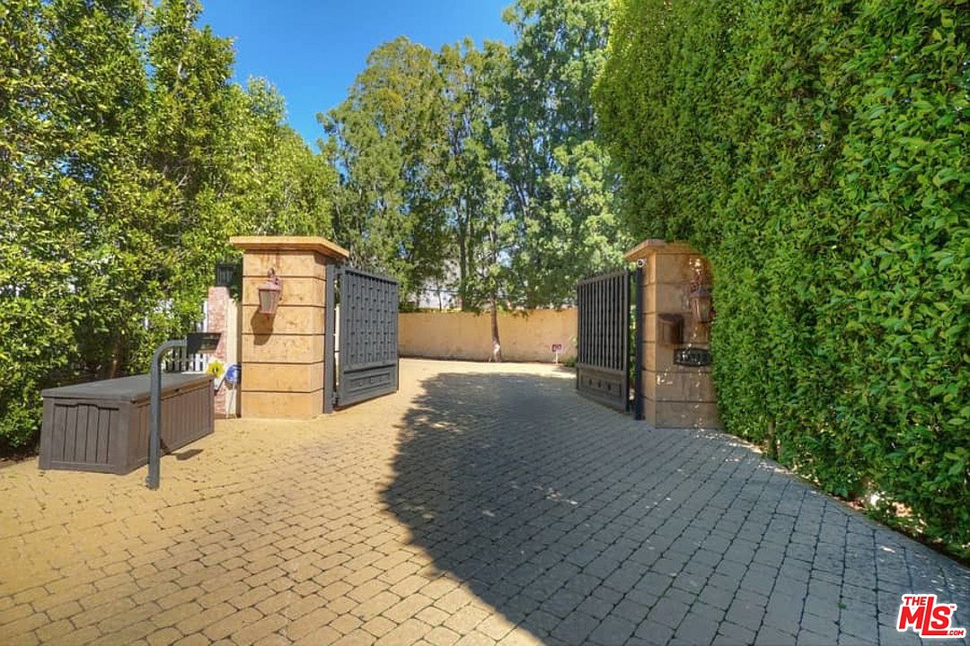 A driveway with brick and stone pavers leading to a gated entrance.