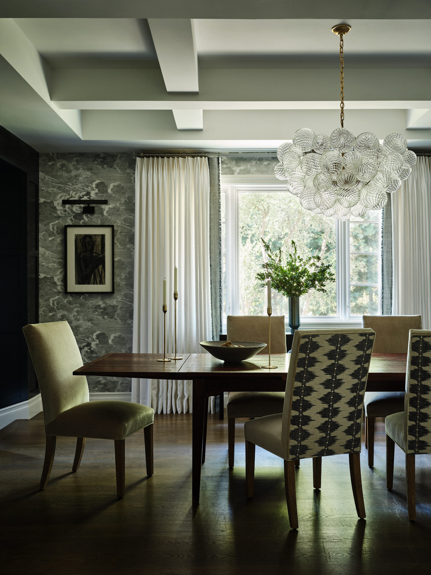 A dining room with a table and chairs, chandelier and windows.