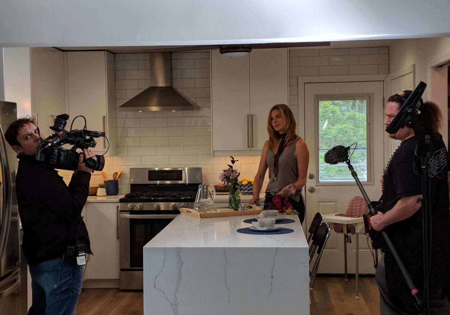 A man and woman are being filmed in the kitchen.